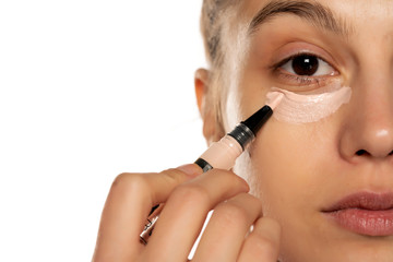 Portrait of young beautiful woman applying concealer with brush