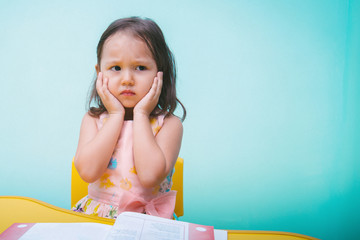 Portrait of a little serious girl on a blue background, with copy space. She is upset, the...
