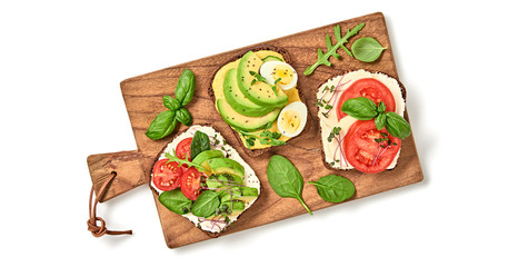 Open sandwiches with vegetables, avocado, tomato, mozzarella, boiled egg and soft cheese. Homemade sandwich with cherry tomato, radish sprouts on wooden board isolated on white, top view