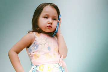 Portrait of an angry child girl talking on a cell phone. Little female kid having a discussion on a smartphone. Children's communication concept with copy space.