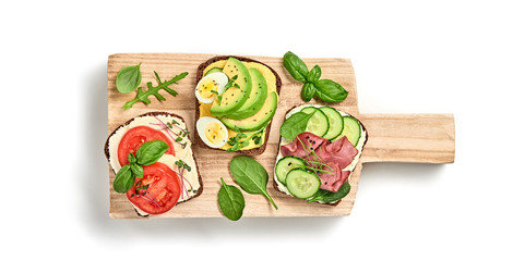 Open sandwiches with avocado, tomato, mozzarella, egg and soft cheese. Fresh sandwich with ham, cucumber on wood isolated on white, top view. Homemade sandwich concept