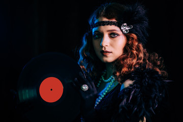Old-fashioned woman dressed in style of Flappers posing with vinyl record on dark background with...