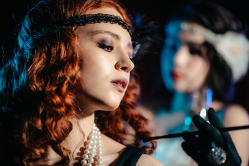 Portrait of young flapper women dressed in style of Great Gatsby posing on dark velours background....