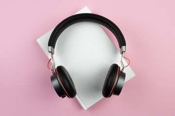 audiobook concept, top view of stereo headphones on hardcover book on pink desktop