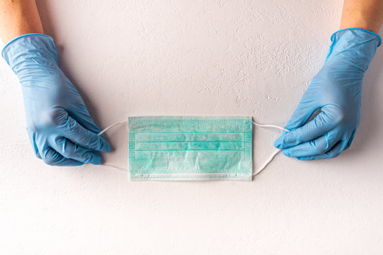 Female Hands In Medical Gloves Holding Protective Face Mask On Light Background. Copy Space