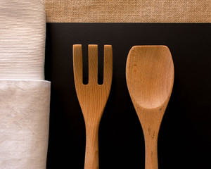 Large natural wood salad servers set on against black table mat with natural table cloth and white napkins