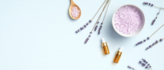 Naklejka na ściany i meble Natural lavender salt and essential oil with lavender flowers on blue background. Organic cosmetic, SPA treatment, body care concept. Flat lay, top view