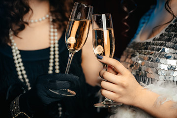 Close up glasses of champagne. Flappers women wearing in style of Roaring Gatsby twenties drinking...