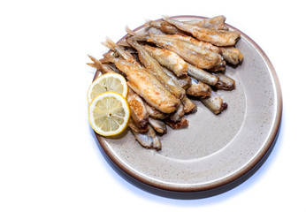 Fried smelt, fish lies on a clay plate, lemon wedges. Top view, copy space