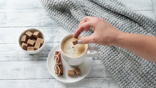 Female hand puts piece of brown sugar in mug with coffee. Cozy autumn composition. Hygge concept. 4K footage