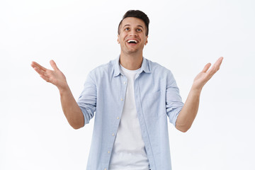 Portrait of blessed happy handsome man thanking god with relief, raising hands and smiling broadly, thankful for miracle, dream came true or wish fulfilled, standing white background cheerful