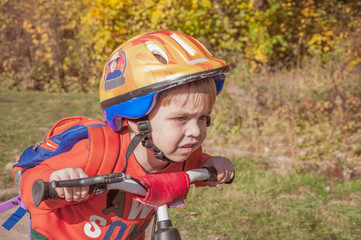 Fototapeta na wymiar A boy in a helmet with a backpack rides a bicycle. He looks carefully ahead. Walk in the park.