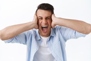 Portrait of distressed and angry young man going insane, shut ears and shouting displeased, feel...