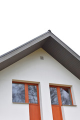 Part of white house with new eaves made of dark brown wooden planks and orange windows with ventilation grid on decorative plaser facade.
