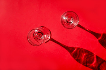 Two empty glasses with shadows on red background in natural sunlight .