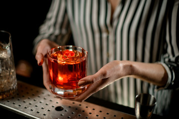 close-up view on old-fashioned glass with cocktail in woman hands at bar