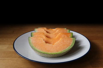 Close up sliced melons in white plate on wooden table.