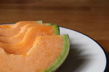 Close up sliced melons in white plate on wooden table.