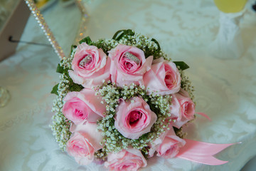 pink ribbon .pink engagement flowers on white table . Bride and groom with Engagement gold rings put on the pink wedding bouquet . Pink engagement bouquet .