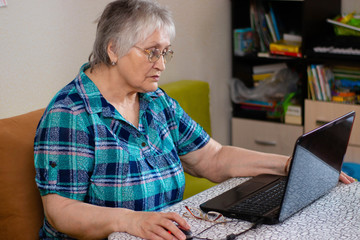 An older woman sits at a laptop. Mastering the older generation of technology by people. Internet communication from home, the photo