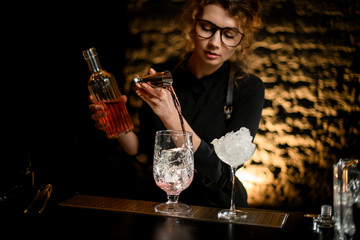 young nice girl barman pours drink from jigger into mixing cup.