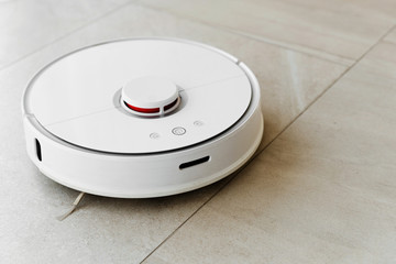 Robot vacuum cleaner during cleaning,white robot vacuum cleaner cleans the floor from debris,home cleaning with an electric vacuum cleaner,vacuum cleaner electric robot cleaning technology