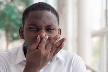 Fototapeta na wymiar African black man covering his nose for bad smell; African black man plugging his nose to display concept of bad smell, bad breath, dirty or filthy thing, rotten stuff, gross fart smell