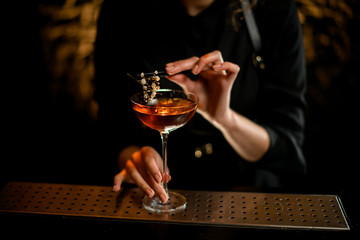 Close-up woman bartender decorates glass with cocktail by white flower.