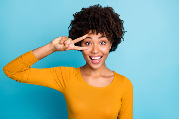 Portrait of excited amazed afro american girl enjoy free time autumn spring holiday enjoy rejoice make v-sign wear good loom sweater isolated over blue color background