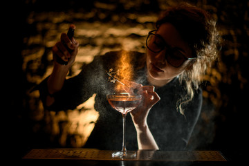 beauty woman bartender decorates illuminated glass with cocktail by white flower and sprinkles on it.