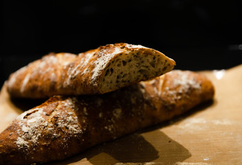 two baked homemade bread lie on the table,homemade baked bread with seeds,baguette sprinkled with flour,fresh bread on a black background,fresh bread texture