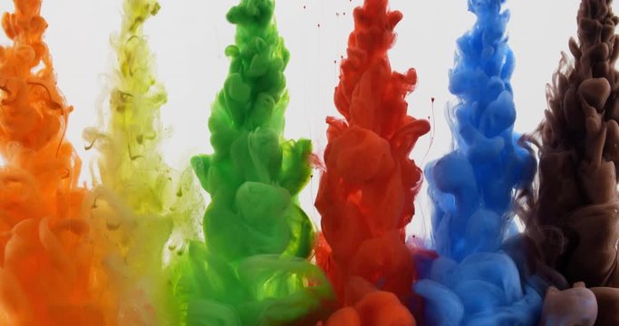 Multicolored rainbow paint drops from above mixing in water, colored smoke clouds spreading underwater on white background, colorful background
