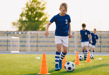 Footballer running with ball on training pitch. Soccer practice for junior level team. School sports field in the background. Football training on sunny summer day