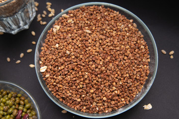 Гречка и другие крупы в стеклянной посуде стоят на сером фоне. Перловая крупа. Бобы. Маш. Красная фасоль.  Вегетарианская еда. Источник белка и угливодов. Диета. Правильное питание. Здоровая еда.