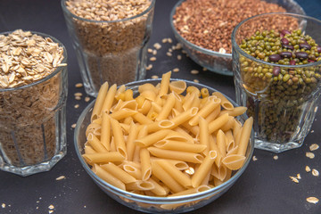 Macaroni and other cereals in glass containers stand on a gray background. Pearl barley. Beans. Mash. Buckwheat. Vegetarian food. Diet. Good nutrition. Healthy food. Horizontal photo. Side view.