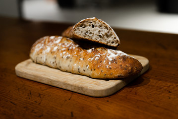 home baked fresh bread lying on a wooden table,two breads lie on a cutting board,branded home-baked bread,baguette with seeds,bran loaf