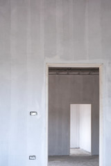 Dimension and perspective view of 2 door frames on cement wall inside of incomplete house construction site, selective focus