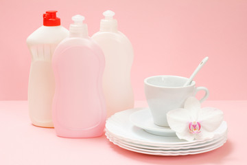 Bottle of dishwashing liquid and utensil on a pink background.