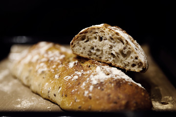 two baked homemade bread lie on the table,homemade baked bread with seeds,baguette sprinkled with flour,fresh bread on a black background,fresh bread texture