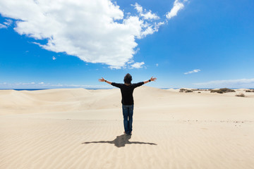 Man with arms wide open on a desert dune landscape. New experiences of freedom traveling around the...