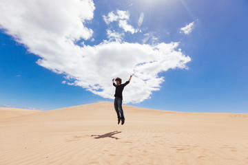 Fototapeta na wymiar Panoramic view of man jumping on a desert dune with blue sky and clouds. New experiences traveling around the world. Travel and holidays concept. Maspalomas natural landscape in Canary Island.