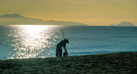 Along the shores of Hoi An, Cua Dai beach in Vietnam, with a lot of best luxury hotels and resorts. Silhouette of a worker with typical conical hat cleaning the sandy beach.