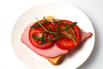 Sandwich of sturgeon, cheese, bread, tomatoes and arugula on a white background on a plate view from the top