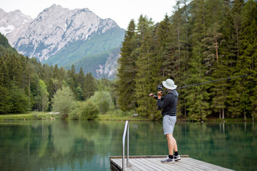 Fototapeta na wymiar Man fishing on the pier in a beautiful lake and forest with mountains.