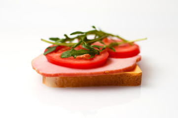 Sandwich made of balyk, cheese, bread, tomatoes and arugula on a white plate side view