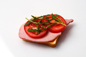 A sandwich of balyk, cheese, bread, tomatoes and arugula on a white plate view from the side and from the top