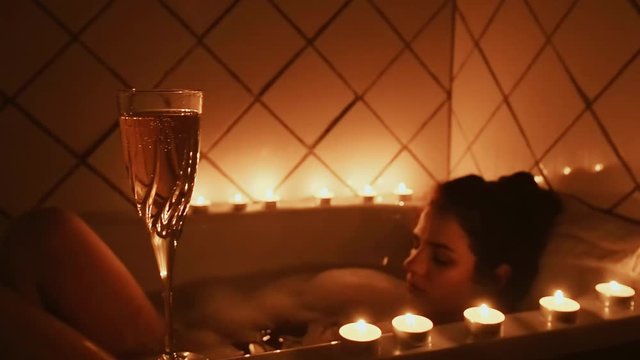 glass of champagne with candles in the bathroom on the background of a young relaxing girl taking a bubble bath