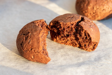Baked cracked round chocolate cookie broken in half on a baking sheet with parchment paper just taken out of the oven. Tea or coffee snack. Selective focus. Closeup view