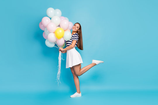 Full length profile photo of beautiful pretty lady good mood bring many air balloons friend birthday event wear striped t-shirt white short skirt footwear isolated blue color background