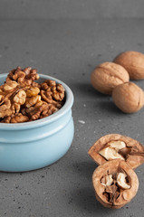 Peeled walnuts in a blue bowl, next to split and whole nuts on a gray background